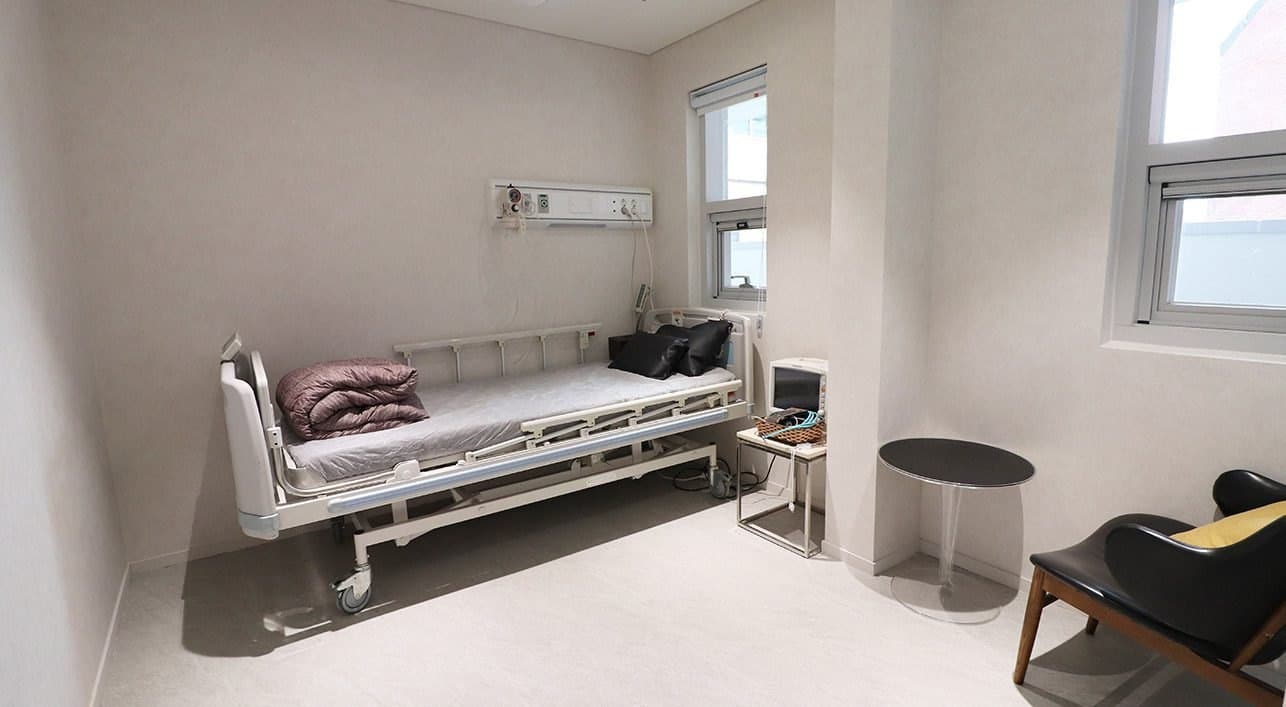 A recovery room with a bed by the window and a wall-mounted medical gas panel